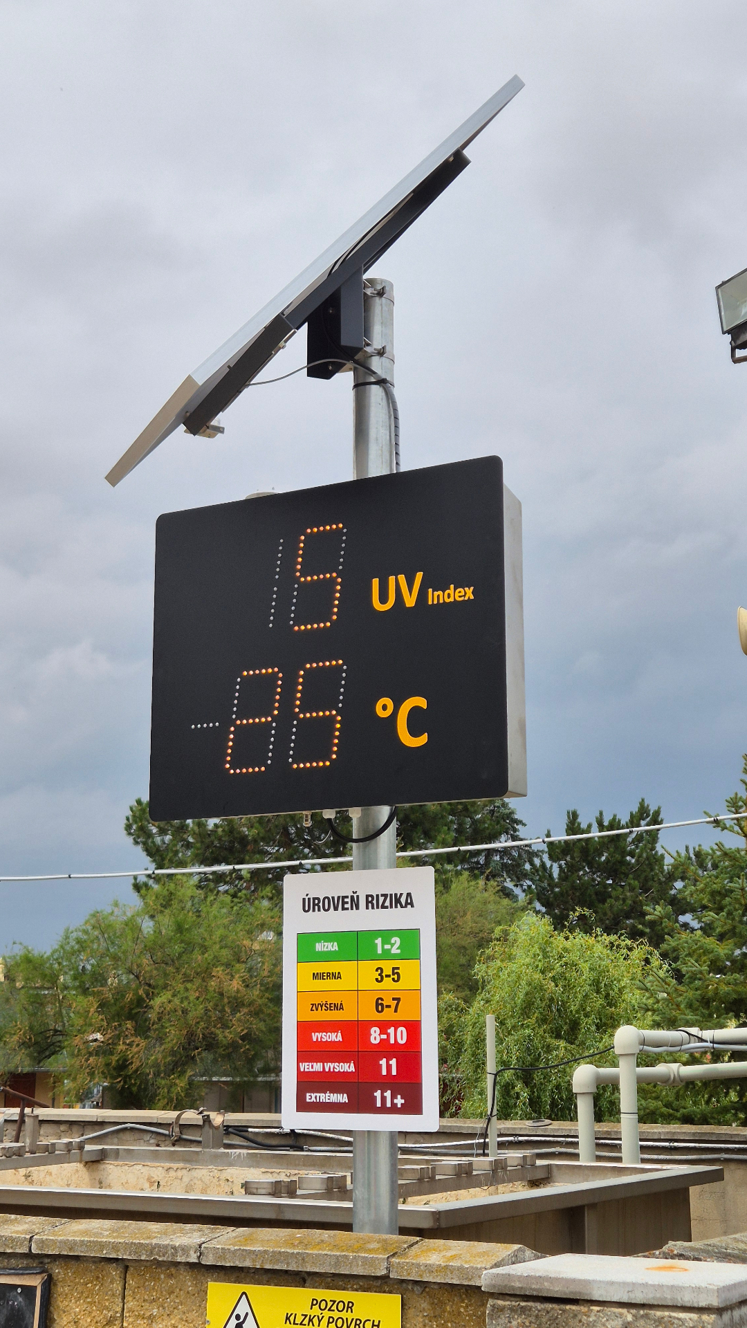 Informačný LED panel BELLIMPEX so solárnym panelom zobrazujúci UV index a teplotu.