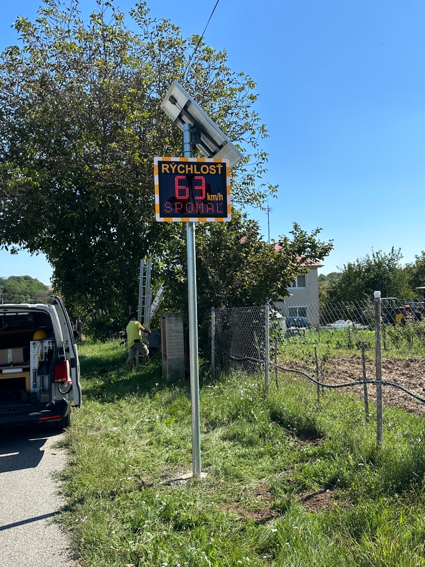 Radarový merač rýchlosti BELLIMPEX s LED zobrazením 63 km/h a výzvou SPOMAĽ v obci.